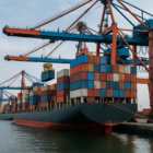 A container ship is being loaded at a busy port, highlighting current supply chain volatility.